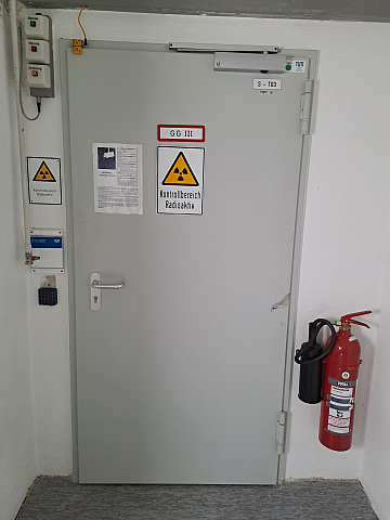Eingang zu einem Kontrollbereich. Die drei Warnlampen rechts oben zeigen den aktuellen Betriebszustand des im Raum hinter der Türe befindlichen Messsystems an.